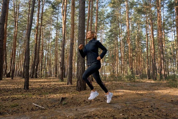 Jonge atletische vrouw joggen in het bos in de zonnige ochtend. Gezond levensstijl concept — Stockfoto