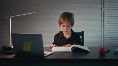 Uzaktan öğrenme, bir çocuk evde bir masada oturup kayın laptopuna bakar. Çevrimiçi eğitim kavramı, ev. Küçük çocuk akşam geç saatte evde ödev yapıyor..