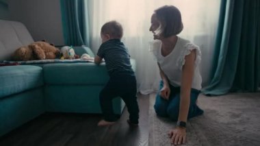 Yakışıklı, gülümseyen çocuk yürümeyi öğreniyor. İlk Bebek Adımları. Bebek ilk adımlarını atıyor.