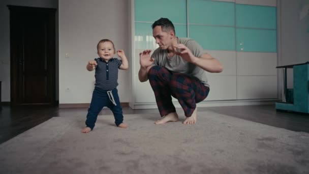 Baby macht erste Schritte mit Vätern Hilfe zu Hause. Vater ermutigt kleinen Sohn zu ersten Schritten zu Hause — Stockvideo