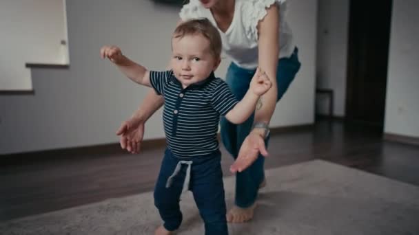 Χαριτωμένο χαμογελαστό αγοράκι που μαθαίνει να περπατάει. Τα πρώτα βήματα του μωρού. Το μωρό κάνει τα πρώτα του βήματα. — Αρχείο Βίντεο