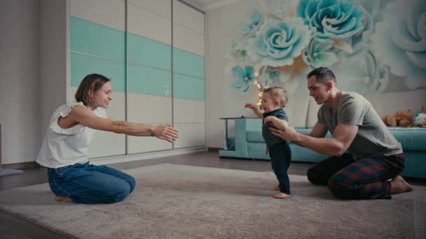 Glückliche Familie lächelt, als Baby die ersten Schritte macht. Familie zu Hause ermutigt Sohn zu ersten Schritten — Stockvideo