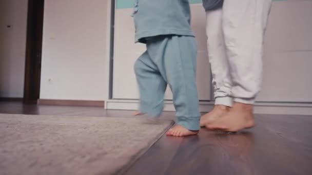 Precioso bebé caucásico biy aprender a caminar dando el primer paso a pie a su madre en casa. Niño caminando por el suelo con el pie descalzo. Lindo niño aprendiendo a caminar. Primeros pasos bebé — Vídeos de Stock