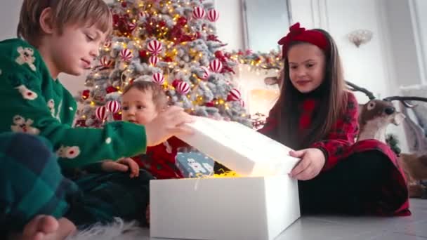 漂亮的男孩和女孩在圣诞树旁玩耍，打开装有礼物的盒子。客厅。房子装修。平安夜家庭概念. — 图库视频影像