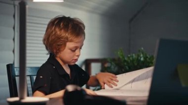 Uzaktan öğrenme, bir çocuk evde bir masada oturup kayın laptopuna bakar. Çevrimiçi eğitim kavramı, ev. Küçük çocuk akşam geç saatte evde ödev yapıyor..