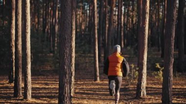 Gündoğumunda sonbahar ormanında koşan genç bir kadın. Yavaş çekim 4k