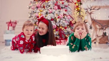 Noel şekeri yiyen iki küçük çocuğun 4K video portresi. El yapımı çikolatalı tatlılar çocukların elinde. Kardeşim Noel ağacının yanında şeker yiyor.