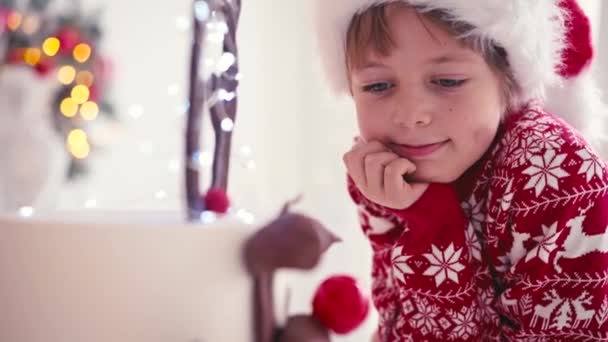 Chłopak siedzi koło świątecznego tortu. Chłopiec czeka na Boże Narodzenie, aby zjeść ciasto — Wideo stockowe