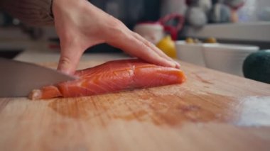 Kadın elleri mutfakta somon filetosu kesiyor. Yakından çekilen eller taze balık kesiyor. Kadın salata yapıyor.