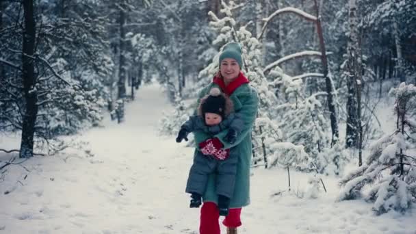Молодая счастливая мать веселится и играет с малышом сыном в снежном лесу зимой — стоковое видео