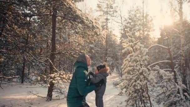 Papá vomita al cielo niño en el bosque de invierno en el fondo de los árboles nevados. — Vídeos de Stock