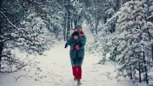 Νεαρή ευτυχισμένη μητέρα διασκεδάζει και παίζει με το παιδί γιο στο χιονισμένο δάσος το χειμώνα — Αρχείο Βίντεο