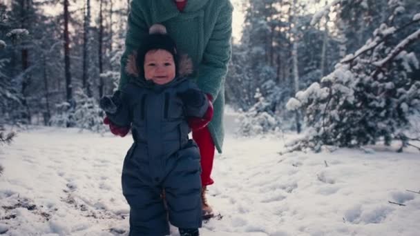 Mother learning her little baby son his first steps in the snow forest. — стоковое видео