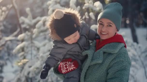 Joven madre feliz divirtiéndose y jugando con su hijo pequeño en el bosque nevado en invierno — Vídeos de Stock