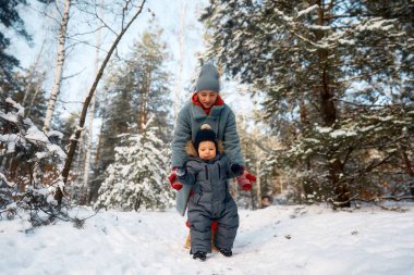 Genç anne ve bebeği karlı ormanda oynuyorlar. Genç anne çok karlı bir günde ormanda bebeğini taşıyor.