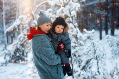 Genç anne ve bebeği karlı ormanda oynuyorlar. Genç anne çok karlı bir günde ormanda bebeğini taşıyor.