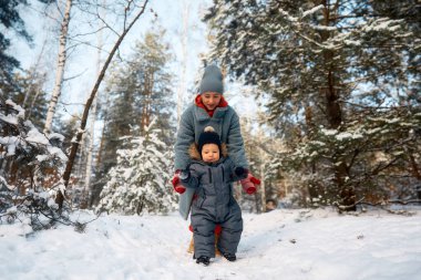 Genç anne ve bebeği karlı ormanda oynuyorlar. Genç anne çok karlı bir günde ormanda bebeğini taşıyor.