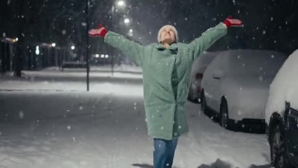 Кинематографический кадр беззаботной счастливой улыбающейся молодой женщины в теплой шляпе взволнован и поражен снегопадом в праздничный зимний вечер.. — стоковое видео