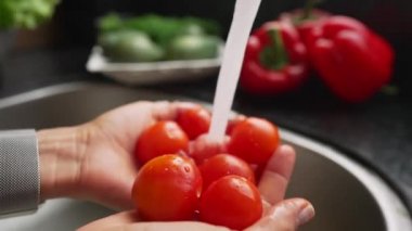 Mutfaktaki su deresinin altında domates yıkayan kadın elleri. Yavaş çekim.