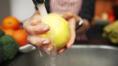 Ayva meyvesini elinde tutan kadın suyun altında yıkayıp temizliyor. Sağlıklı beslenme. Yavaş çekim..
