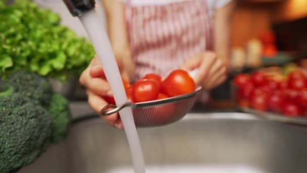 Mains féminines lavant un tomate sous un ruisseau d'eau à la cuisine. — Video