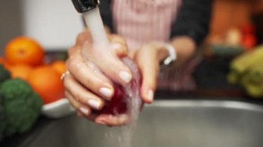 Kadın elleri elmaları lavaboda suyun altında yıkıyor. Kırmızı elmaları kadın ellerinde yıkamak, ağır çekim.