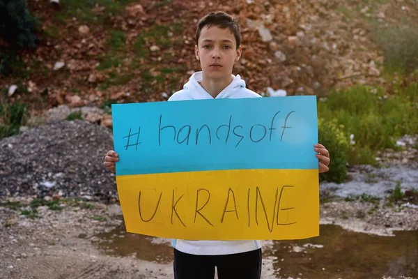 Portrait de garçon ukrainien enfant près du bâtiment détruit montrant bannière avec massage texte mains hors de l'Ukraine. Je demande de l'aide. Crise, guerre, pas de paix, arrêter l'agression du pays Russie — Photo gratuite