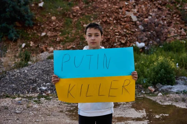 Retrato del niño ucraniano cerca del edificio destruido mostrando pancarta con texto de masaje Putin Killer. Pidiendo ayuda. Crisis, guerra, no paz, detener la agresión de Rusia país — Foto de stock gratis