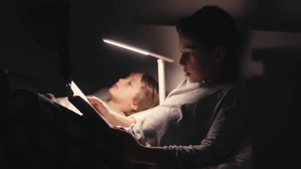 Αγόρια ξαπλωμένα στο κρεβάτι στο σκοτάδι και διαβάζοντας βιβλίο. — Αρχείο Βίντεο