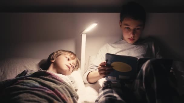 Meninos deitados na cama no escuro e livro de leitura. — Vídeo de Stock