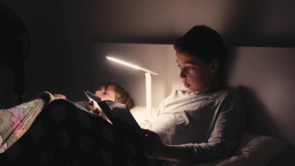 Niños acostados en la cama en la oscuridad y leyendo libro. — Vídeo de stock