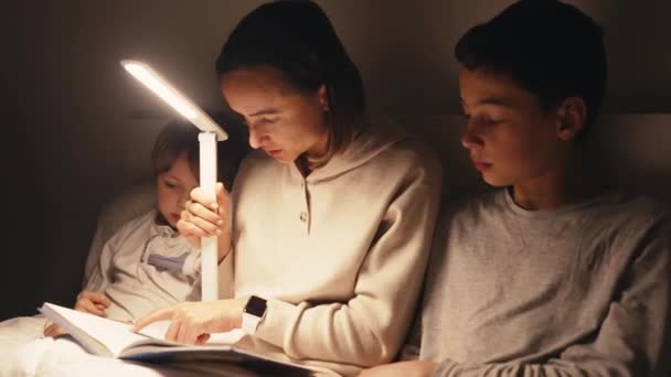 Mamá leyendo un libro para los niños. Madre e hijos por la noche en el dormitorio y leyendo el libro antes de acostarse. — Vídeo de stock