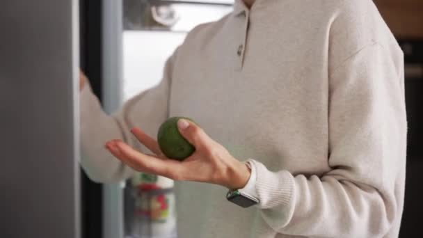 Uma mulher tira comida do frigorífico. Mulher tomar abacate. — Vídeo de Stock