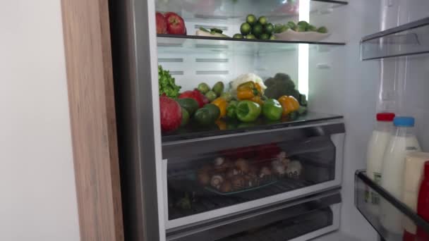 Niño abriendo la puerta del refrigerador mientras está de pie en la cocina. Refrigerador lleno de frutas y verduras. concepto de estilo de vida saludable — Vídeos de Stock