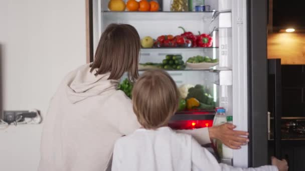 부엌에 서서 냉장고 문을 여는 소년. 과일 과 채소로 만든 냉장고를 사용하 십시오. 건강 한 생활 방식 — 비디오