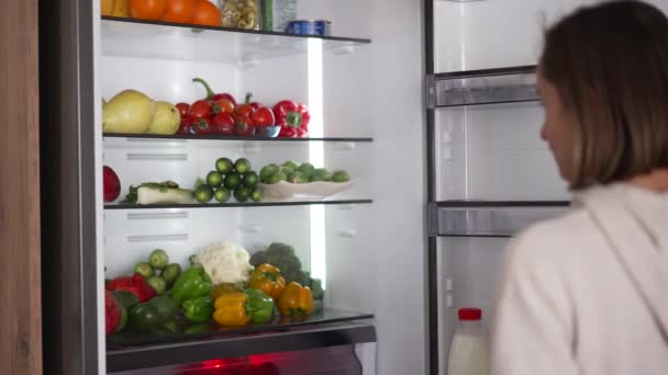 Mujer tomando comida cruda del refrigerador. Refrigerador lleno de comida saludable. frutas y hortalizas. — Vídeos de Stock