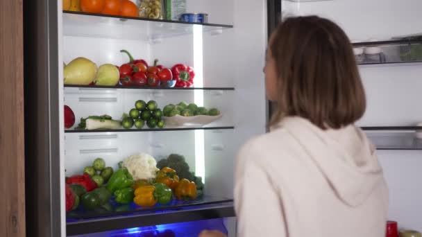 Mujer tomando comida cruda del refrigerador. Refrigerador lleno de comida saludable. frutas y hortalizas. — Vídeos de Stock