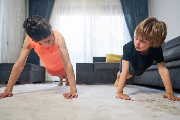 Δύο αγόρια αδέλφια παίζουν σπορ στη φωτεινή κουζίνα στο σπίτι. Ασκήσεις στο σπίτι. Μείνε σπίτι. Οικογενειακή αντίληψη. Δύο αγόρια κάνουν πους απς. — Φωτογραφία Αρχείου