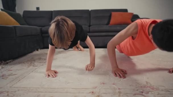 Twee jongens broers sporten thuis in de lichte keuken. Thuistrainingen. Blijf thuis. Familie concept.Twee jongens doen push-ups — Stockvideo