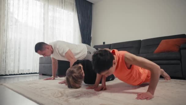 Padre con hijos haciendo ejercicio en casa. Padre y dos hijos haciendo deportes en la alfombra en la sala de estar en casa — Vídeos de Stock