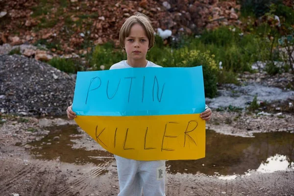 Retrato del niño ucraniano cerca del edificio destruido mostrando pancarta con texto de masaje Putin Killer. Pidiendo ayuda. Crisis, guerra, no paz, detener la agresión de Rusia país —  Fotos de Stock