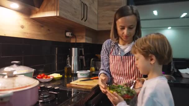 Kaukázusi anya és fia vacsorát készítenek otthon. Aranyos fiú segít a szüleinek, míg boldog nő a háztartási konyhában. Családi kapcsolatok. — Stock videók