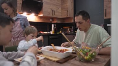 Evde yemek yerken genç mutlu aile sohbeti.