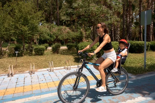 Arka planda bisiklete binen aktif anne ve çocuk. Bisikletli beyaz kadın ve erkek bebek.