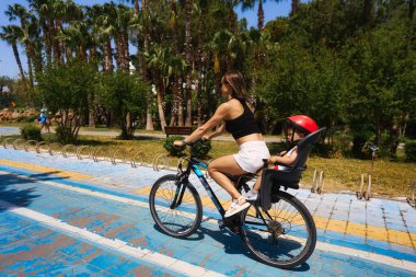 Arka planda bisiklete binen aktif anne ve çocuk. Bisikletli beyaz kadın ve erkek bebek.