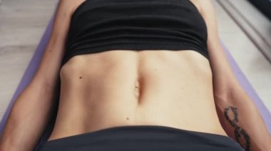 Diastasis recti 'yi kendi göbeğinde nasıl kontrol edeceğini. Anti-selülit masajı. Yüzü tanınmaz halde. Diastasis 'i olan bir kadın siyah spor giysisiyle yerde yatıyor.