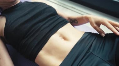 Diastasis recti 'yi kendi göbeğinde nasıl kontrol edeceğini. Anti-selülit masajı. Yüzü tanınmaz halde. Diastasis 'i olan bir kadın siyah spor giysisiyle yerde yatıyor.