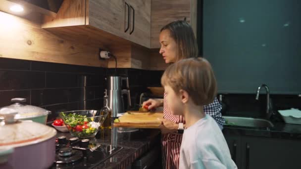 Biała matka i syn przygotowują razem kolację w domu. Słodki chłopiec pomaga rodzicom podczas szczęśliwej kobiety w kuchni domowej. Stosunki rodzinne. — Wideo stockowe