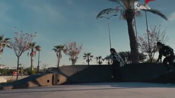 若いカップルは、ポンプトラックや現代的なスタイルのスケートパークでスケートボードをします。ポンプトラックで何百万人ものスケーターの追跡ショット — ストック動画