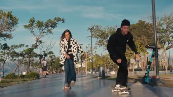 Hipster couple skateboarding. Young couple skateboarding in the street. Couple having fun with skateboard on beach — Vídeos de Stock